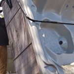 A man wearing a hat and brown pants stands outside, tackling a hot tub removal by lifting a large hot tub on its side next to a wooden fence.