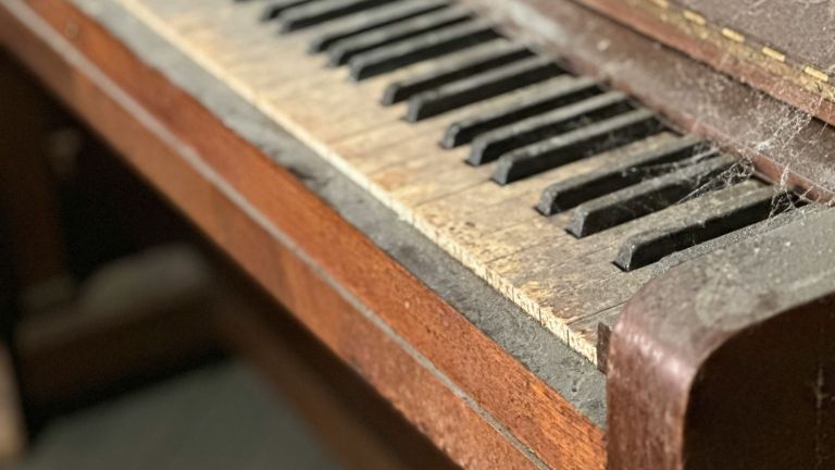 Close-up of dusty, old wooden piano keys, some worn and discolored, with visible cobwebs and accumulated dirt, indicating long-term neglect and disuse.