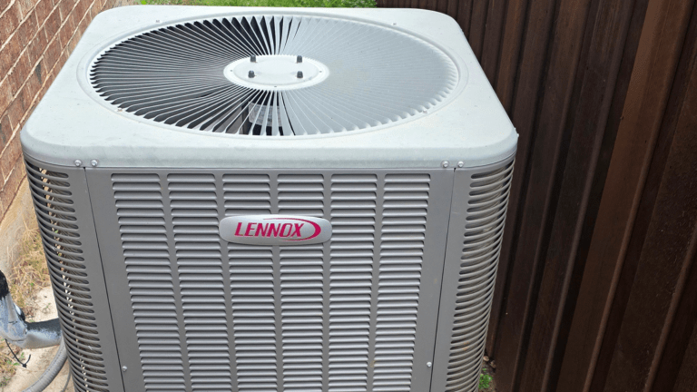 A Lennox outdoor air conditioning unit sits next to a brick wall and a wooden fence in TX, with a visible fan on top and ventilation grilles on the sides, ready for appliance removal in Arlington if needed.