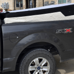 A gray pickup truck with an STX badge is parked on a street, its bed overloaded with a mattress for mattress removal in Arlington, TX by Arlington Junk Removal Service. The mattress sticks out over the edge, barely secured by the tonneau cover.