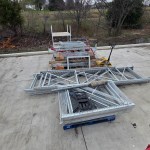 Metal scaffolding pieces and construction materials are stacked on a concrete surface outdoors, with leafless trees and cloudy skies in the background—ideal for scrap metal removal in Dallas,TX by Arlington Junk Removal Service.